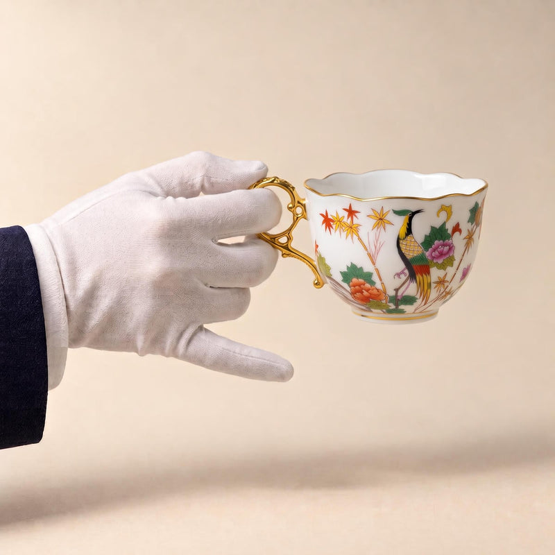 Gloved hand holding a polychrome bird teacup